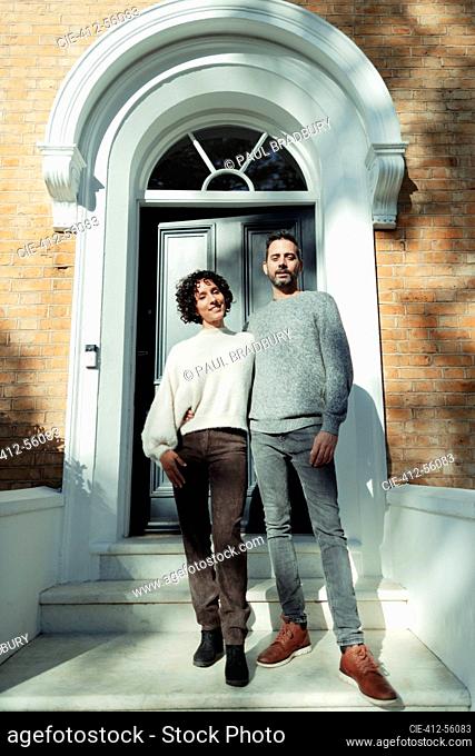 Portrait confident couple at arched front door on sunny house stoop