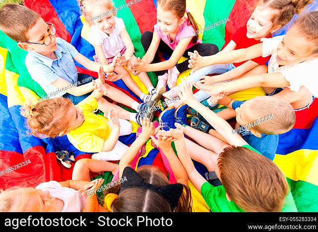 Group of children siting in a circle putting their hands together, laughing and having fun. Summer camp concept