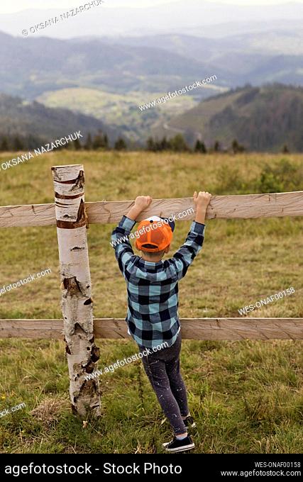 Boy wearing cap playing by fence at farm