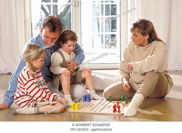 indoor, full-figure, family with 2 children sits on the floor in front of the window playing ludo  - GERMANY, 11/03/2005