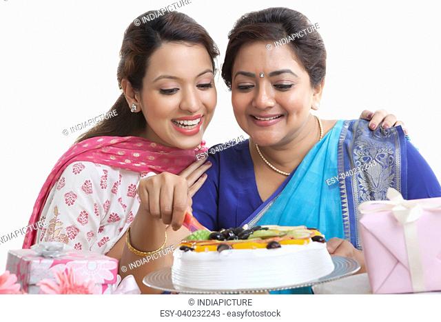 Woman cutting birthday cake while daughter looks on