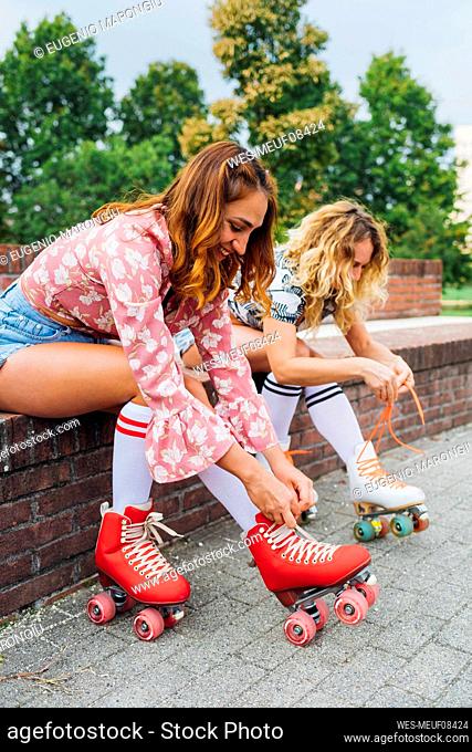 Smiling woman with friend tying lace of roller skates