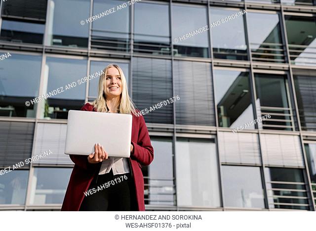 Blond businesswoman with laptop in the background of modern office building