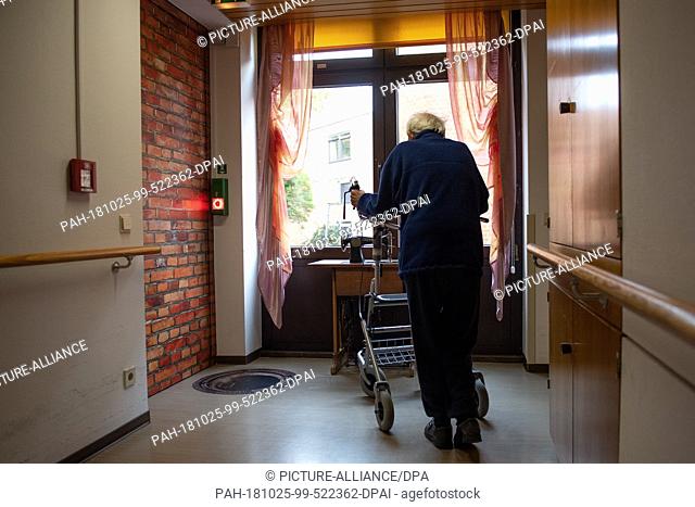 16 October 2018, Hessen, Hofgeismar: A resident with a rollator stands in a corridor of the Altenhilfe Gesundbrunnen in front of a door with photo wallpaper of...