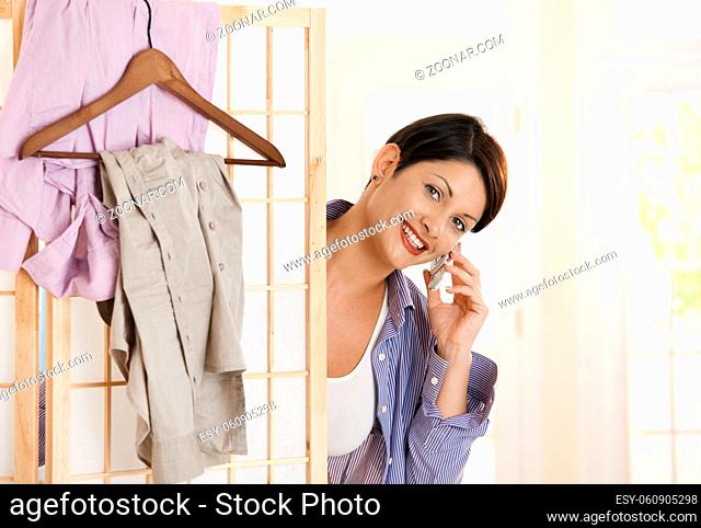 Happy young woman talking on mobile while dressing up, smiling