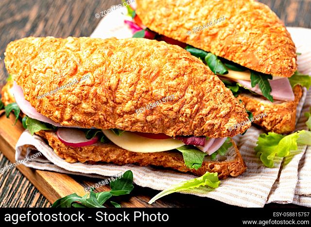fresh submarine sandwich with ham, cheese, bacon, tomatoes, lettuce, on wooden cutting board