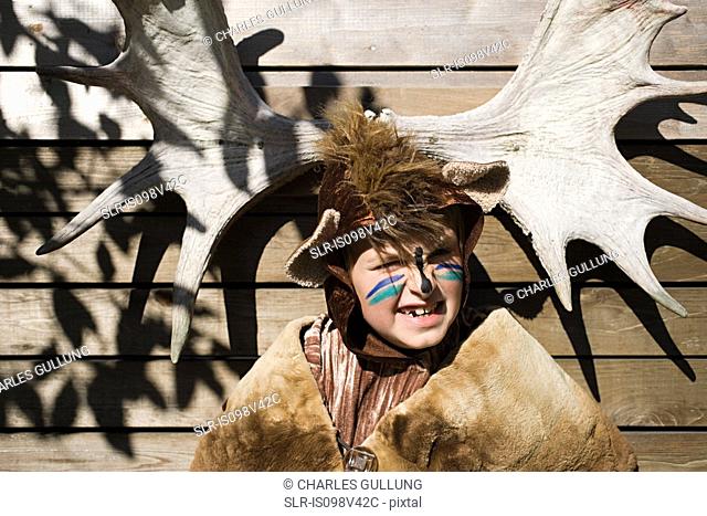 Boy dressed up as bear in front of moose antlers