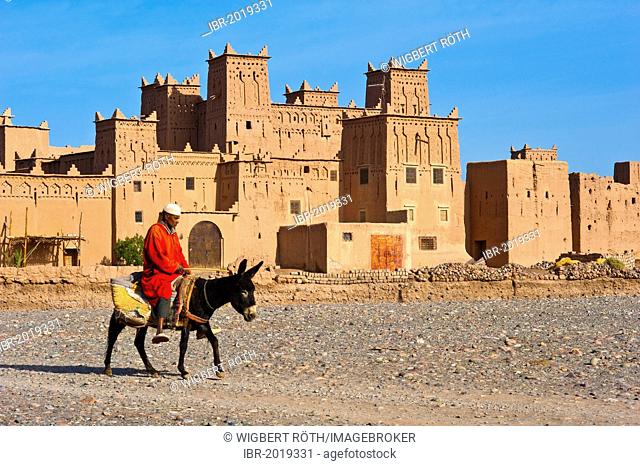 Berber riding on a donkey in front of the Amerhidil Kasbah, mud fortress, residential Berber castle, Tighremt, Skoura, Dades Valley, southern Morocco, Morocco