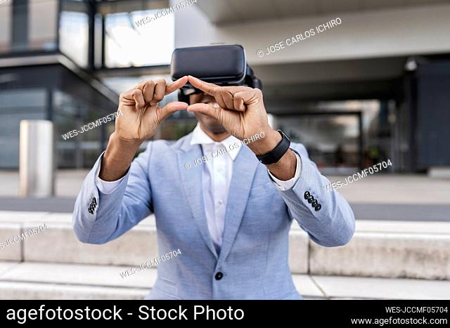 Businessman wearing virtual reality simulator gesturing sitting on steps in front of building