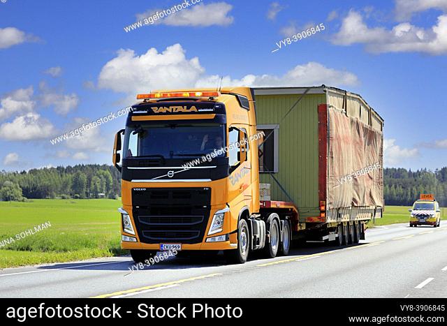 Yellow Volvo FH truck semi trailer Rantala transports portable cabin as oversize load, escort vehicle follows. Jokioinen, Finland. June 15, 2020