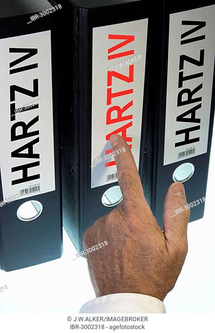 Hand pointing to a ring binder labeled Hartz IV, German term for long-term unemployment benefits, symbolic image