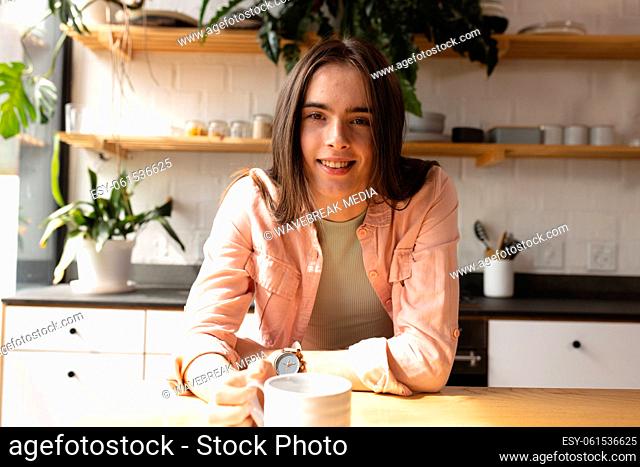 Portrait of non-binary trans woman with coffee cup smiling in the kitchen at home