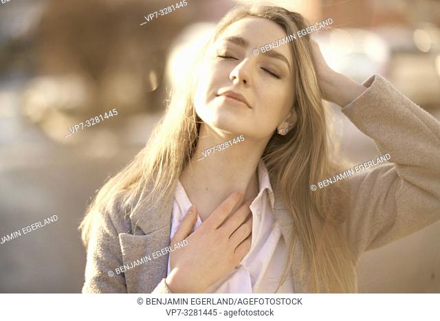 young woman outdoors with closed eyes enjoying sunlight, in Cottbus, Brandenburg, Germany