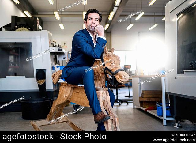 Pensive businessman on wooden rocking horse in a factory