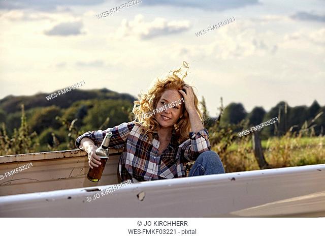 Woman sitting on pick up truck having a beer