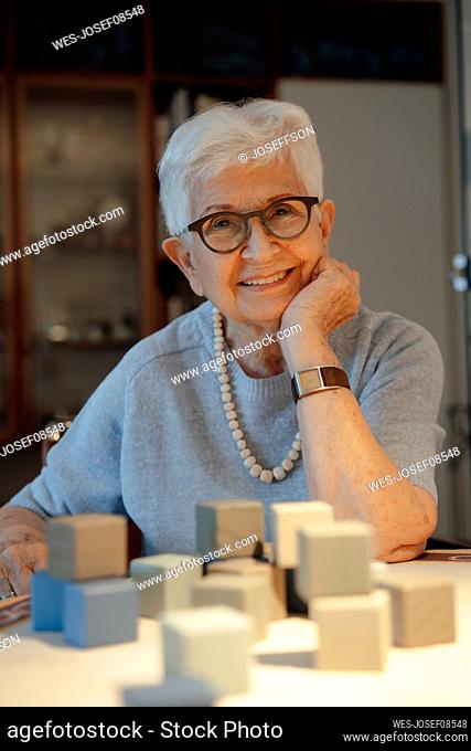 Happy senior woman with toy blocks sitting at table at home