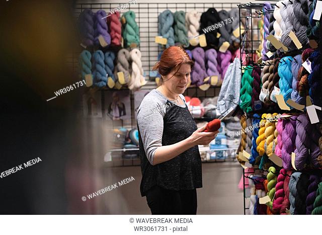 Woman looking at yarn while using digital tablet