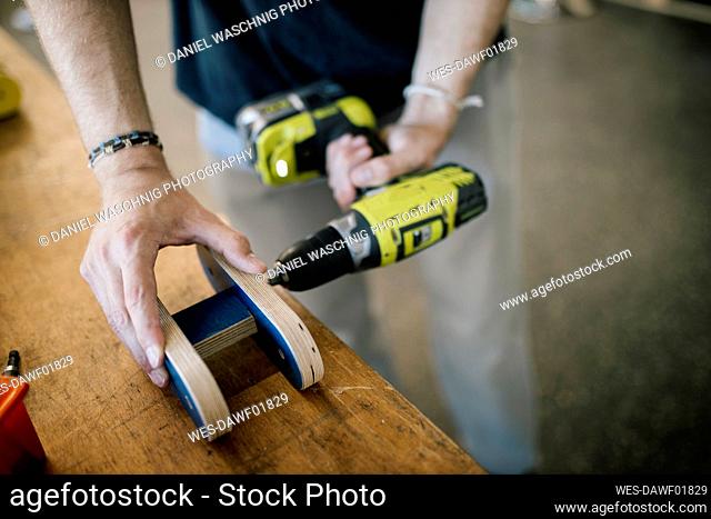 Craftsman making hole in wood material with drill machine on table at workshop