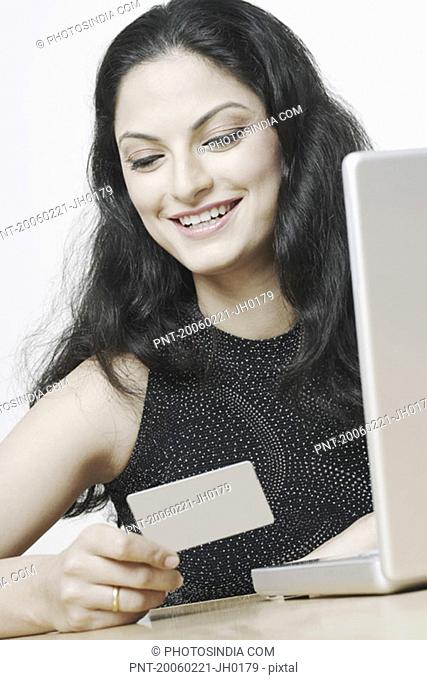 Close-up of a young woman sitting in front of a laptop holding a credit card