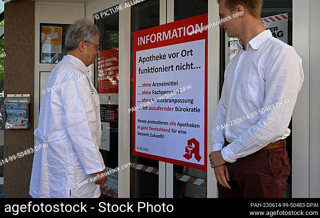 14 June 2023, Baden-Württemberg, Weilimdorf: Christoph (l) and John Gulde from Solitude Apotheke stand in front of protest posters in front of the closed...