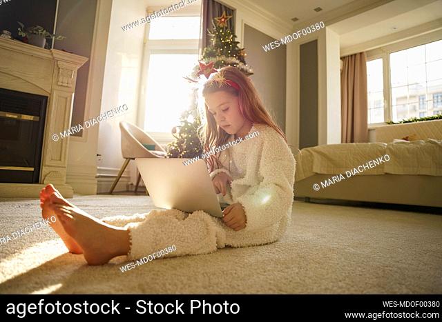 Girl sitting on carpet using laptop in bedroom at home
