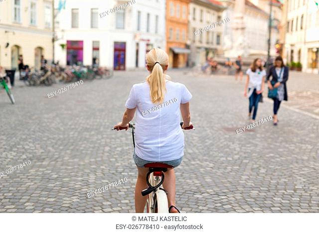Rear view of beautiful blond caucasian woman riding cruiser bike in Ljubljana city center