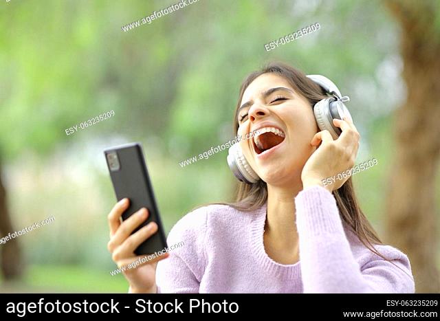 Happy teen singing in a park listening music with headphones and phone