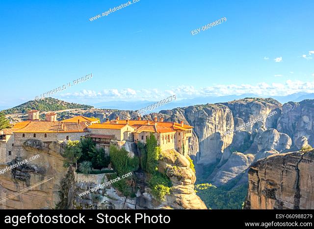 Greece. Clear summer day in Meteora. Several buildings of a rock monastery with red roofs and clouds on the horizon