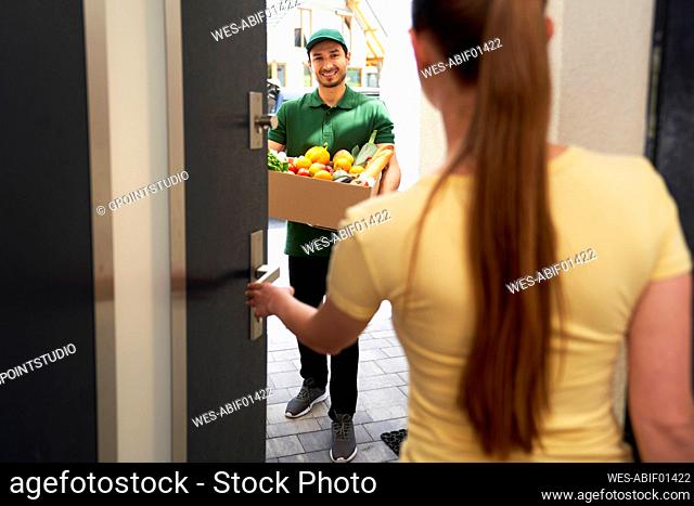 Smiling deliveryman holding vegetable box while standing at entrance