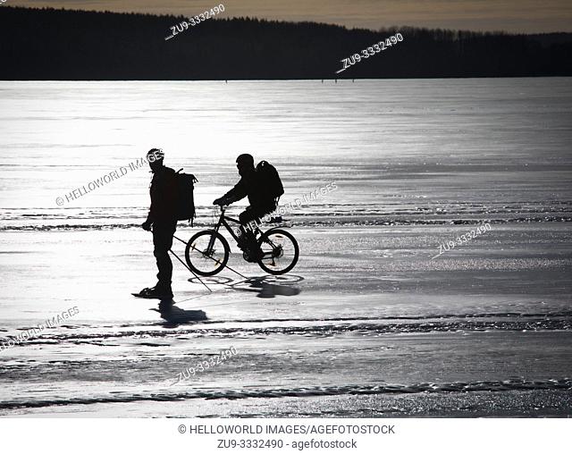 Cyclist and long distance ice skater silhouetted on frozen Lake Malaren, Sweden, Scandinavia