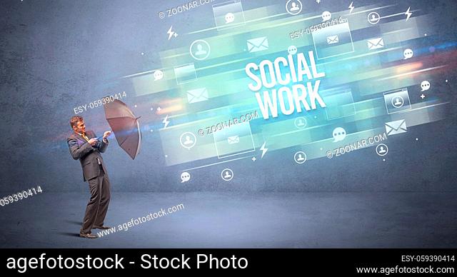 Handsome businessman defending with umbrella from SOCIAL WORK inscription, new age media concept