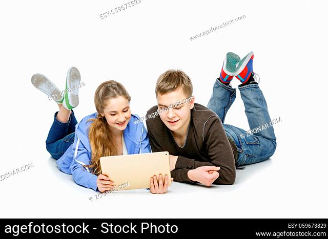 Beautiful teen age boy and girl in casual clothes holding tablet. School children sitting back to back. Isolated on white background. Copy space