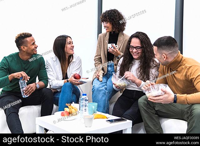 Smiling male and female colleagues talking while having food and drink in work place canteen