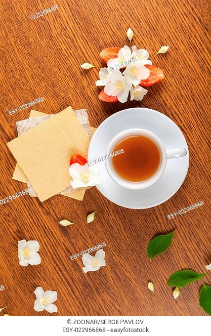 white cup of green tea. jasmine flowers with strawberry halves. texture blank for writing. still life