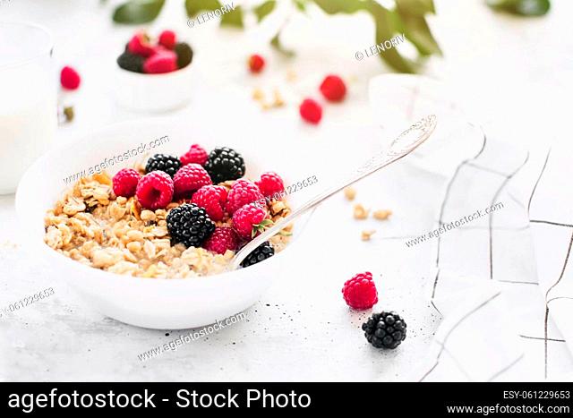 Morning healthy breakfast, white bowl full with granola, muesli, raspberry, blackberry on gray concrete table. Healthy eating, eco, bio food concept