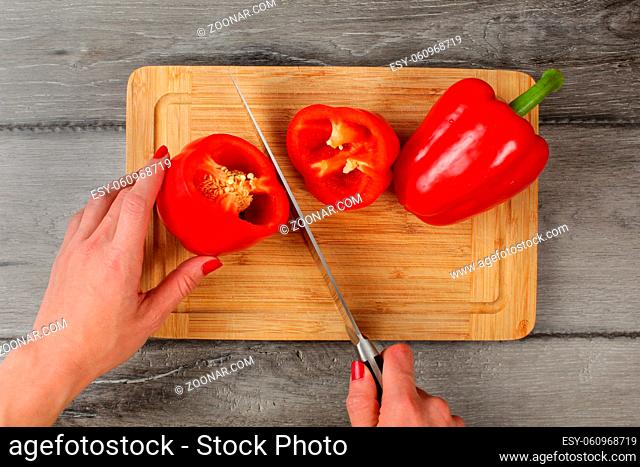 Tabletop view, woman hands cutting red bell pepper with chefs knife on chopping board