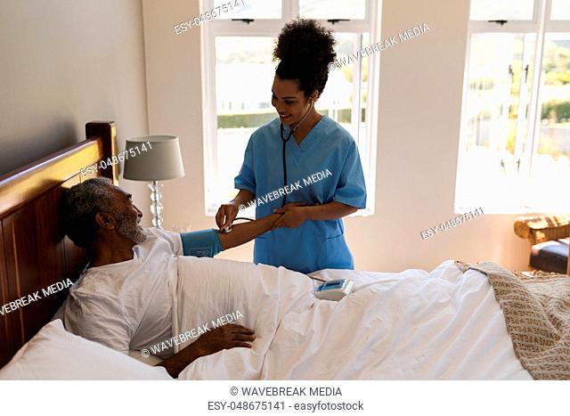 Female doctor measuring blood pressure of senior man in bedroom