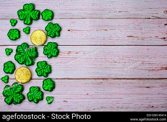 Glitter Covered Four Leaf Clovers and Coins Filling One Half of the Frame on a white Wooden Background