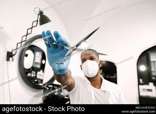 Barber wearing surgical mask and reusable gloves holding scissors
