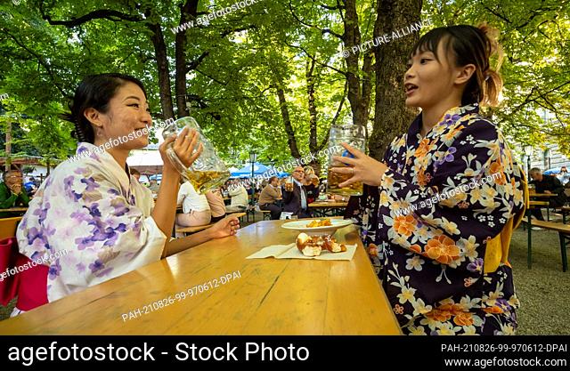 25 August 2021, Bavaria, Munich: The two Japanese women Sakura Suzuki (l) and Imho Uchitani, who are both from Tokyo, drink a Maß beer at Wiener Platz in...
