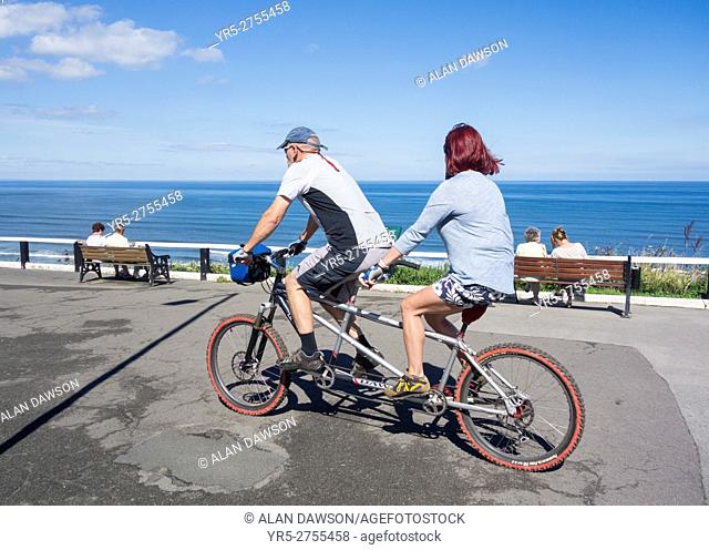Couple riding a Tandem on Saltburn`s top promenade on a summer`s day. Saltburn by the sea, North Yorkshire, England, United Kingdom