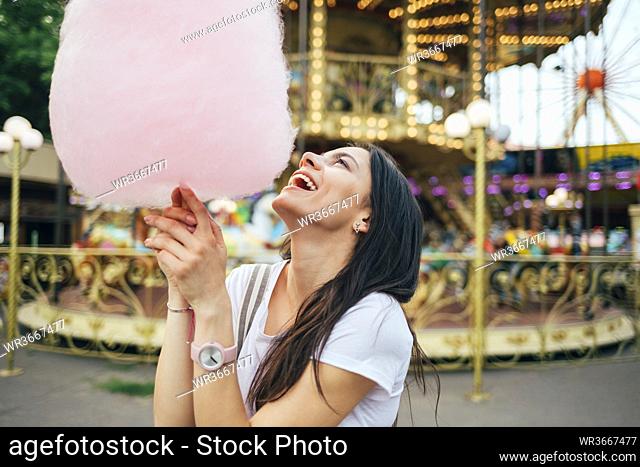 Happy young woman holding cotton candy standing in amusement park