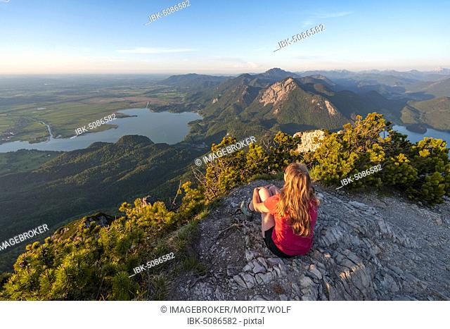 Young woman sitting at the summit, view from Herzogstand to Lake Kochel, Jochberg and Lake Walchen, Alpine foothills, Alps, Upper Bavaria, Bavaria, Germany