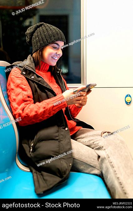 Happy young woman using smart phone sitting in tram