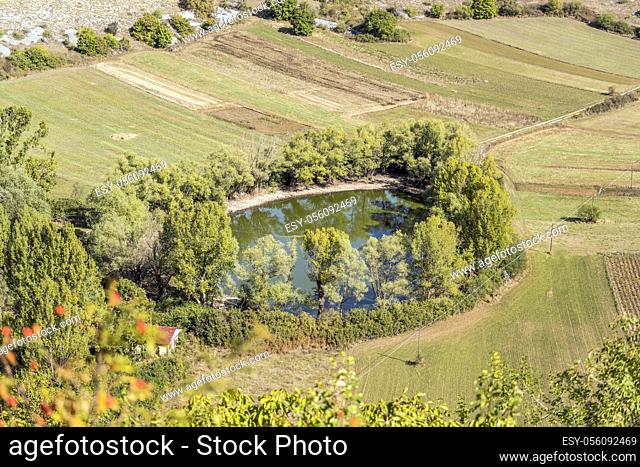 round pond surrounded by trees in green upland, shot in bright light near Calascio, L'Aquila, Abruzzo, Italy