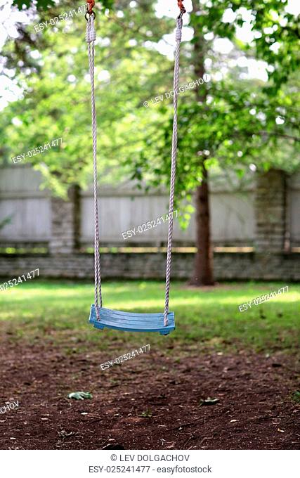 childhood concept - empty wooden swing hanging in summer garden