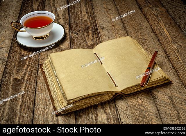 antique leather-bound journal with decked edge handmade paper pages and a stylish pen on a rustic wooden table with a cup of tea, journaling concept