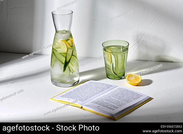glass of water with lemon and cucumber and book