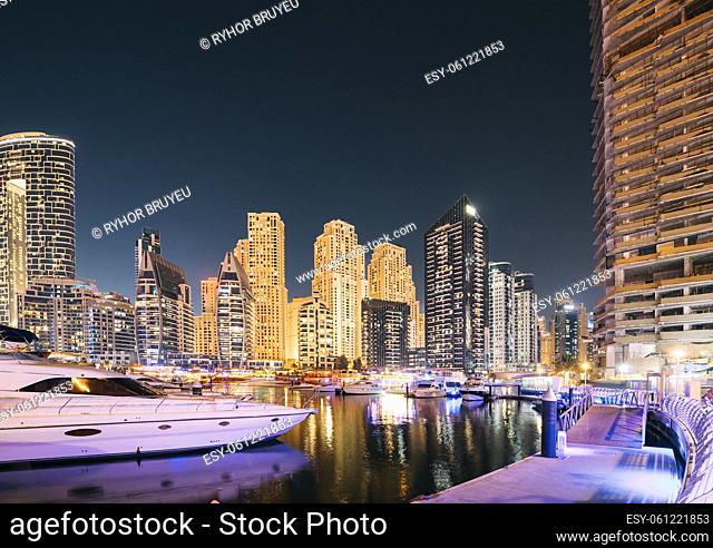 Dubai Marina Port, UAE, United Arab Emirates - Jetty With Many Moored Yachts In Evening Night Illuminations. Night View Of Dubai Marina Skyline