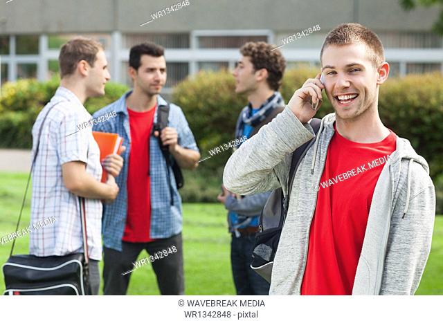 Happy male student on the phone in front of his classmates outside